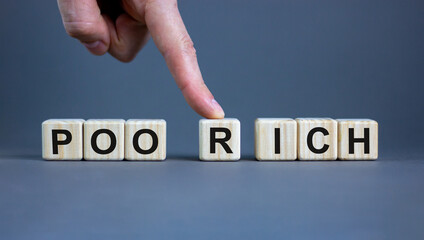 Male hand pushes the cube with the letter R from the word 'poor' to the word 'rich'. Beautiful grey background, copy space. Concept.