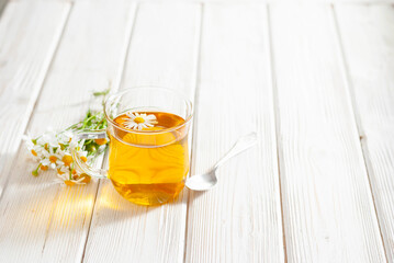 Cup of herbal tea with chamomile flowers on the white wooden background. Natural organic...