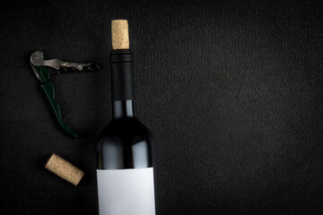 A bottle of red wine, corkscrew and wine corks on black Background, copyspsce. Winemaking  concept.