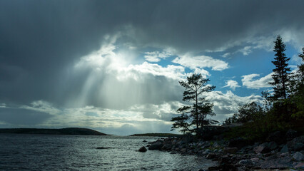 Rays of sunlight break through the clouds. Seascape with Islands. Northern nature. Spruce on a rocky shore. Light phenomenon
