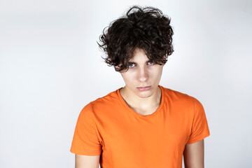 Upset handsome teenage boy in an orange T-shirt on a light background, the guy is in a bad mood because he quarreled with his parents