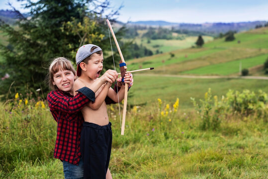 In nature in the mountains, a girl teaches her brother to shoot a bow, they shoot an arrow together, the brother is happy that his sister spends time with him