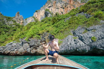 Fototapeta na wymiar An active man on thai traditional longtail Boat is ready to snorkel and dive, Phi phi Islands, Thailand