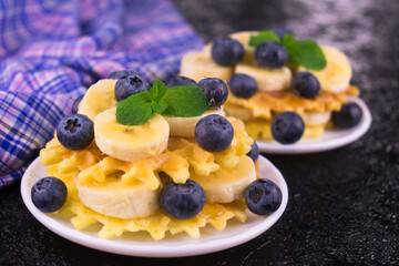 
Waffles with banana and blueberries topped with maple syrup.
Close-up.