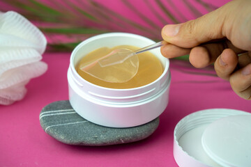 golden under eyes patches in a white container, anti aging skin care, female body care background, pink backdrop