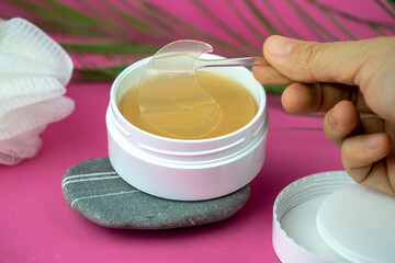 golden under eyes patches in a white container, anti aging skin care, female body care background, pink backdrop