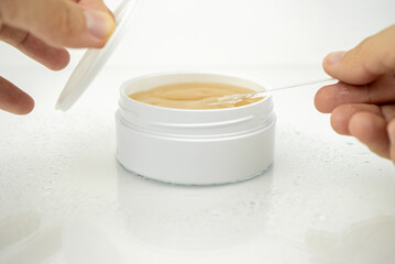 take golden under eyes patches with special spoon from a white container, anti aging skin care, white wet background
