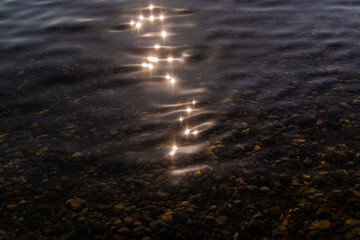 sun glare and colorful  gold pebbles in the clear blue water of lake baikal, ripples, shore, summer