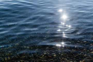 sun glare and colorful  pebbles in the clear blue water of lake baikal, ripples, shore, summer