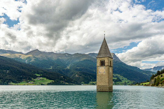 The top of the old bell tower of Curon (Graun) emerges from the waters of Lake Resia, against a dramatic sky, South Tyrol, Italy