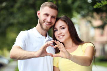Happy young couple showing heart by hands in the park