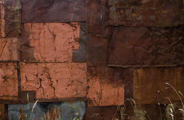Dry grass near the rust and oxidized wall. Old iron panel. The wall of rusted plates. Grunge rusted metal abstract texture. Rusted metal wall. Rusty metal surface with streaks of rust.