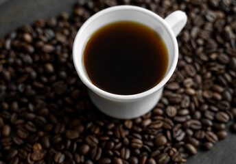 White cup of coffee with roasted coffee beans background. Mug of black coffee.