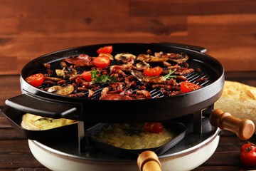 Delicious traditional Swiss melted raclette cheese served in individual skillets with salami and bacon