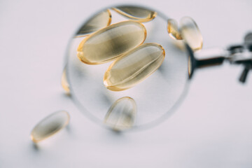 yellow transparent omega 3 capsules under a magnifying glass. vitamin development concept
