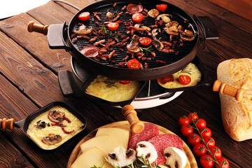 Delicious traditional Swiss melted raclette cheese served in individual skillets with salami and...