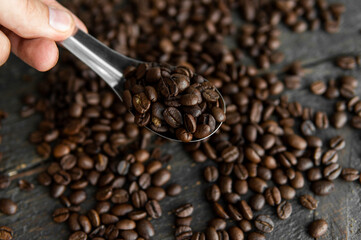 Fresh roasted arabica coffee beans in a metal spoon and scattered coffee beans on a wooden table.
