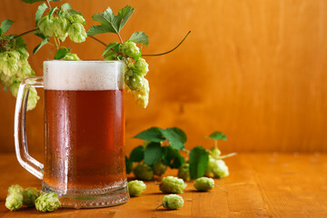 A mug of hopped light beer on a wooden table with green hops