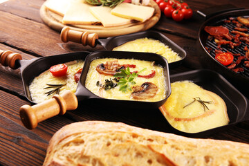 Delicious traditional Swiss melted raclette cheese served in individual skillets with salami and...