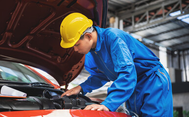 Asian mechanic wearing a safety helmet, checking the car engine in an opened hood car. Auto car repair service center. Professional service.