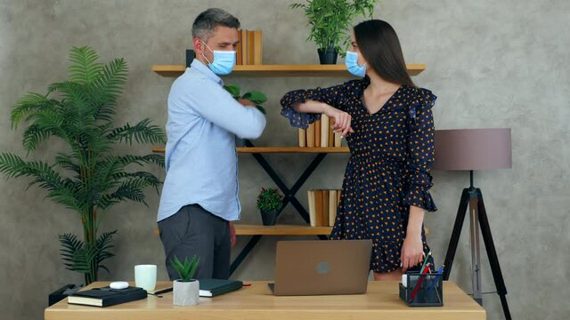 Woman and man wear protective medical masks on faces greet elbows employees working together in an office preparing presentation for meeting. Manager shows report to businessman on laptop computer