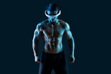 Fototapeta na wymiar Muscular model sports young man in glasses of virtual reality on dark background. Fashion portrait of strong brutal guy. Sexy torso. Male flexing his muscles. VR. Blue neon light.