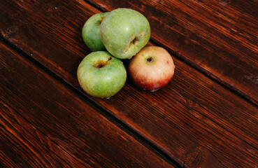 Fresh autumn Apple harvest on the kitchen countertop. Four fresh apples lie on a wooden table. A textured mahogany wood background and fruit lie on it.