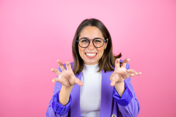 Young beautiful business woman over isolated pink background smiling funny doing claw gesture as...