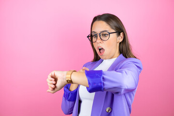 Young beautiful business woman over isolated pink background surprised and pointing his watch...