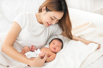 Beautiful asian women mother long hair in the white pajamas. mom looking at newborn infant with love, while a baby sleeping in her arm with warm, safe, comforted resting on the clean bed.