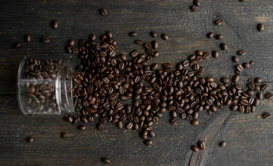 Roasted fresh arabica coffee beans scattered on a table from a little jar on a wooden table. Fresh...