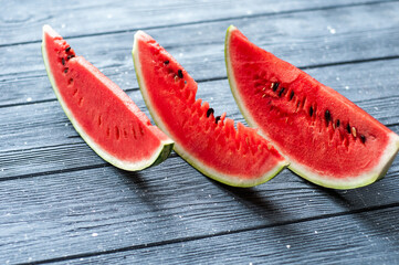 Fresh sliced watermelon and watermelon pieces on a wooden background.