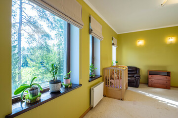 Luxury interior of bedroom in modern apartment. Leather chair. Baby bed. Wooden dresser. Green flowers on windowsill.
