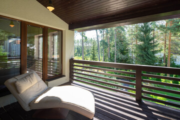 Cozy lounge chair on wooden terrace. Luxury cottage. Green forest at sunny day.