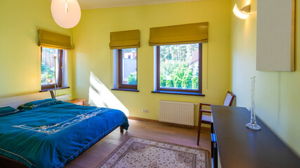 Contemporary interior of bedroom with yellow walls in cottage. Wooden furniture. Cozy bed.