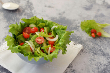 fresh salad tomatoes, cucumber, peppers, green lettuce on a gray background in a neutral salad bowl