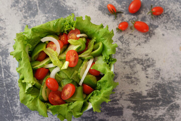fresh salad tomatoes, cucumber, peppers, green lettuce on a gray background in a neutral salad bowl