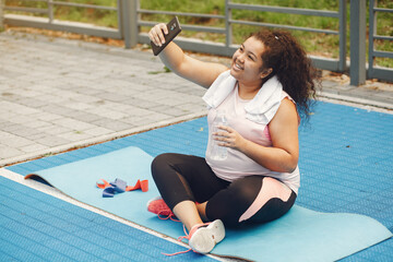 Young tired plus size woman. Girl training in a park. Woman sitting on a mat.