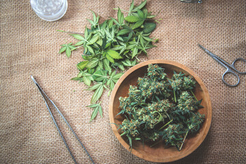 Cropped cannabis buds and leaves in wooden plates on the fabric surface of the table