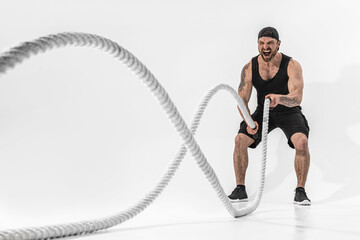 Attractive muscular man working out with heavy ropes. Photo of handsome man in sportswear isolated...