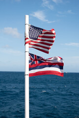 American flag and Hawaiian flag waving on the back on a boat at a tropical beach in Hawaii Waikiki with deep blue ocean 