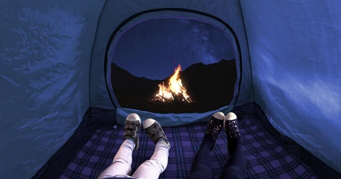 Two kids inside on a camping tent looking at the mountains during the night