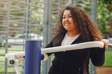 Young tired plus size woman. Girl training in a park. Woman in a black sportsuit.