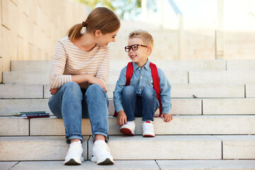 first day at school. mother and little schoolboy son sit on the stairs together.