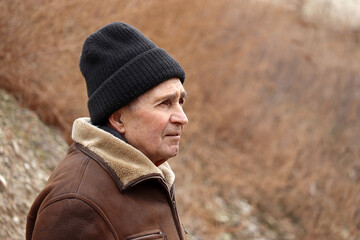 Portrait of elderly man standing on autumn rural background. Concept of cold weather, life in...