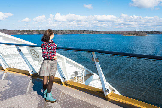 Beautiful slender girl traveler on the upper deck of cruise ship. Asian young woman dressed in red plaid shirt and short skirt in luxury cruise. Elegant happy woman look at ocean relax on luxury liner