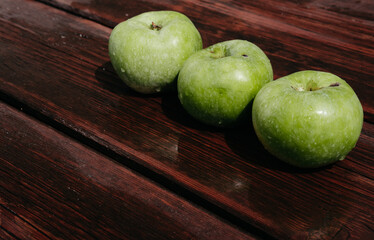 Fresh autumn Apple harvest on the kitchen countertop. Three fresh green apples lie in a row on a wooden table. A textured mahogany wood background and fruit lie on it.