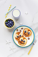 un food for kids - cute smiling faces on sweet pancakes for breakfast with bananas, fresh blueberries and blackberries. Creative cooking for children