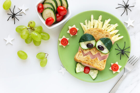 Naklejki Fun food for kids - cute smiling monster face sandwich with ham and cheese, served with fresh tomatoes and cucumbers