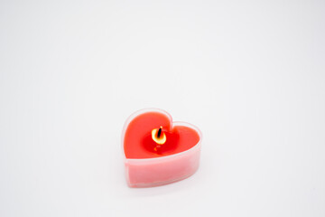 A red candle in the shape of a heart is burning, and glass hearts are lying around. Concept of love, Valentines day, passion